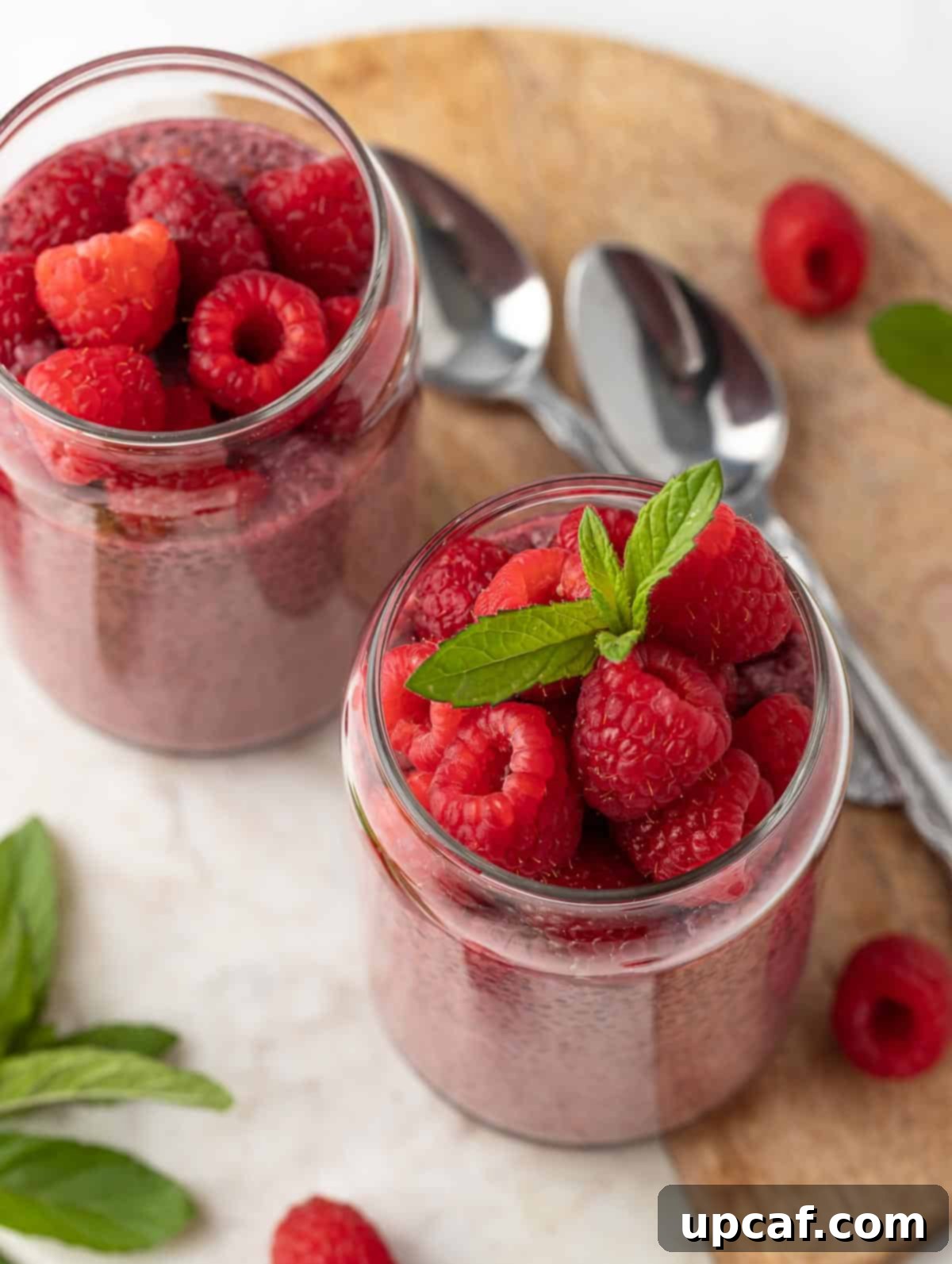 Vibrant Raspberry Chia Pudding 7 Top shot of Raspberry Protein Chia Seed Pudding, garnished with fresh raspberries and a mint leaf, served alongside two spoons on a elegant marble surface.