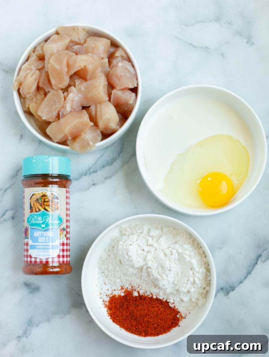 Ingredients laid out for crispy chicken bites: chicken tenderloin, flour, seasoning, egg, heavy cream, and canola oil.