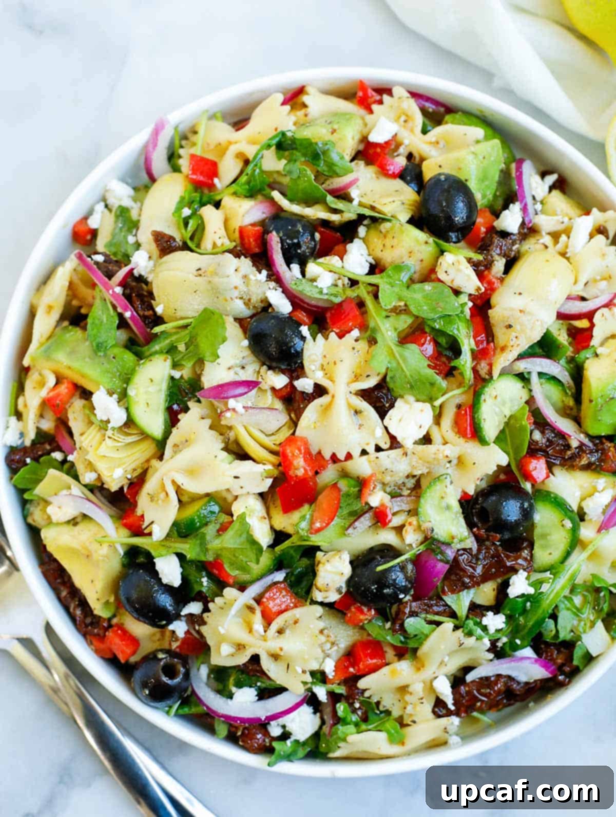 Vibrant lemon herb Mediterranean pasta salad served in a elegant white bowl, garnished with fresh lemon slices and herbs.