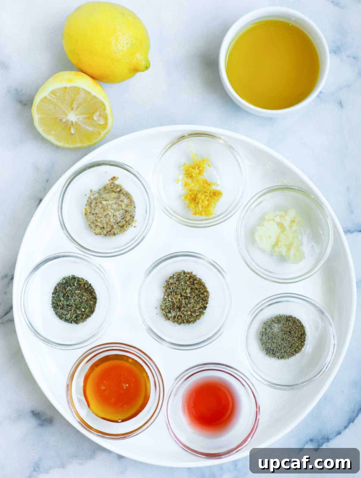 Collection of fresh ingredients for a lemon herb dressing, including whole lemons, olive oil bottle, and a bunch of fresh herbs.