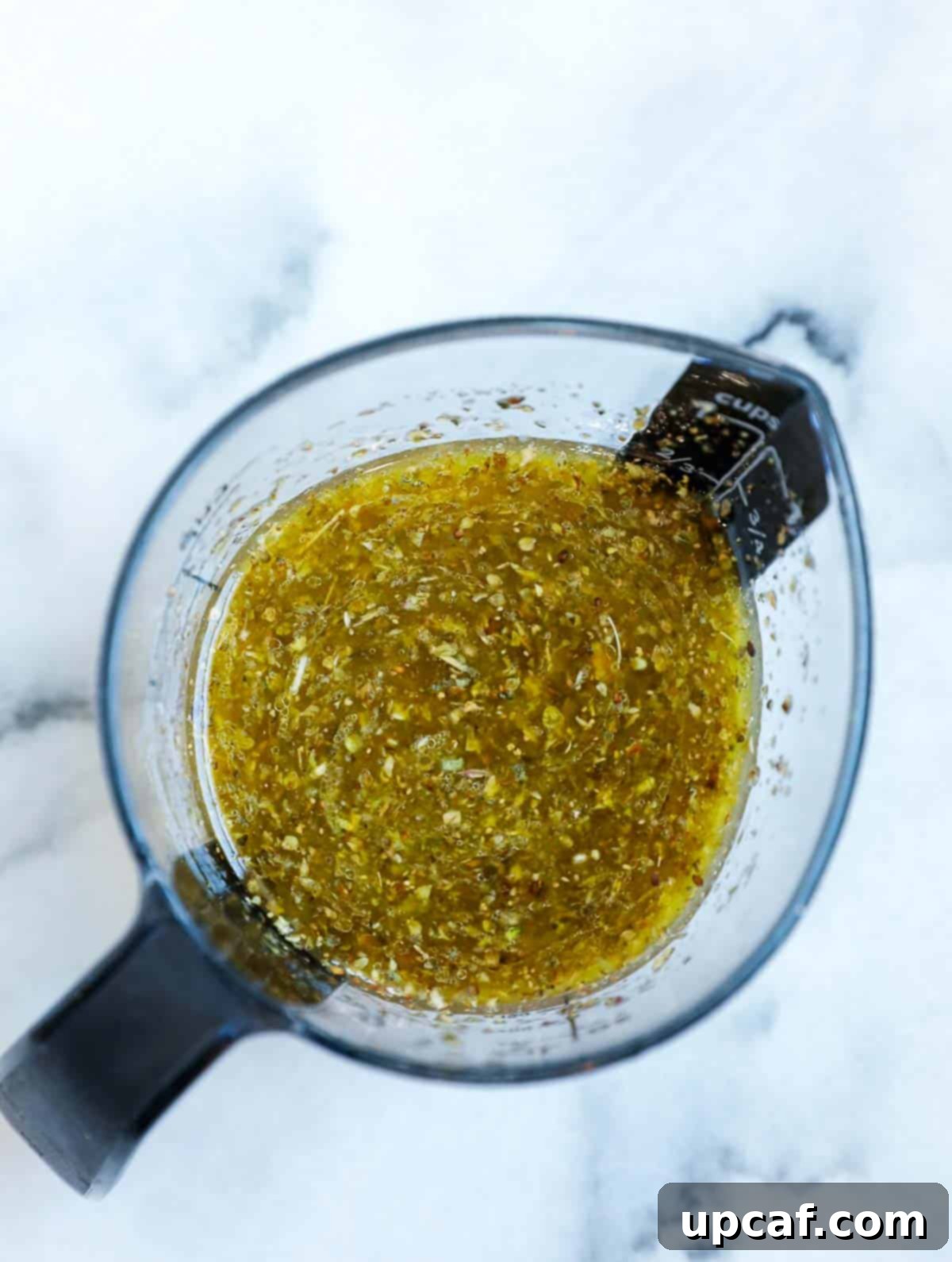 Homemade lemon herb dressing mixed thoroughly in a clear measuring cup.