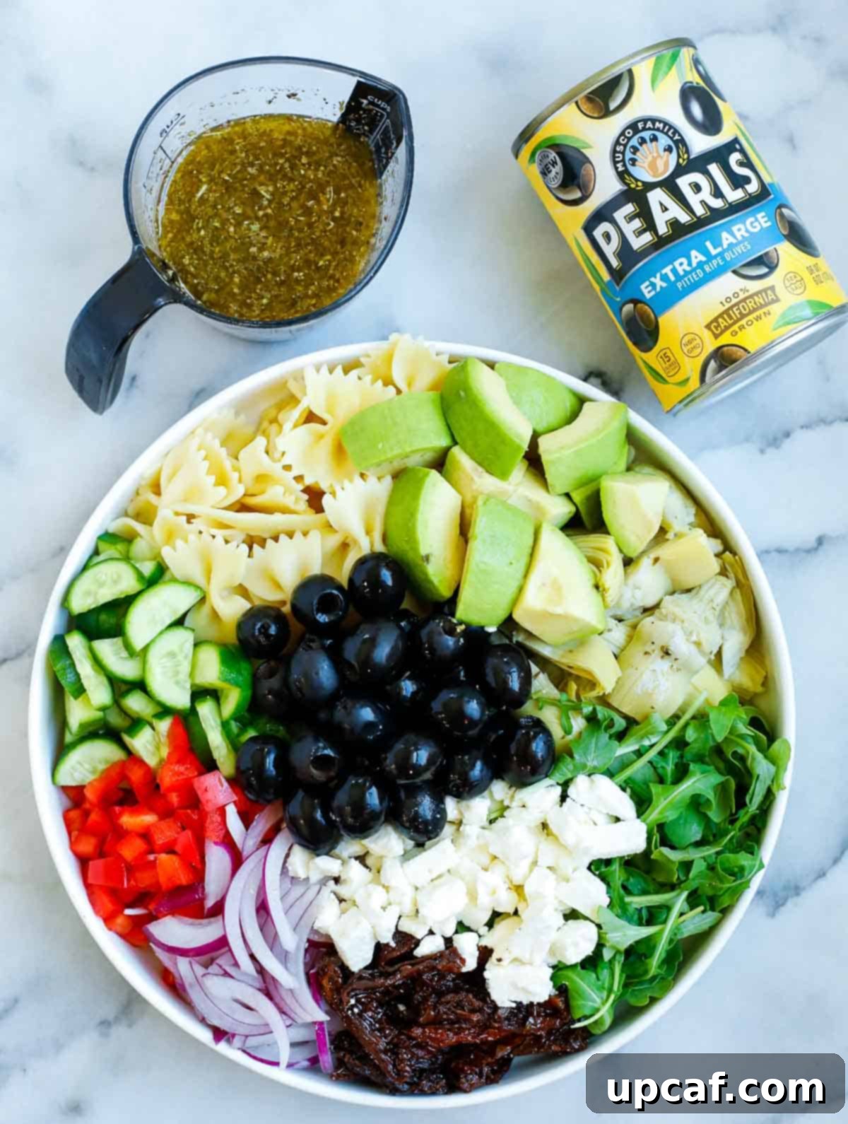 A large bowl filled with colorful Mediterranean salad ingredients before the dressing is added.