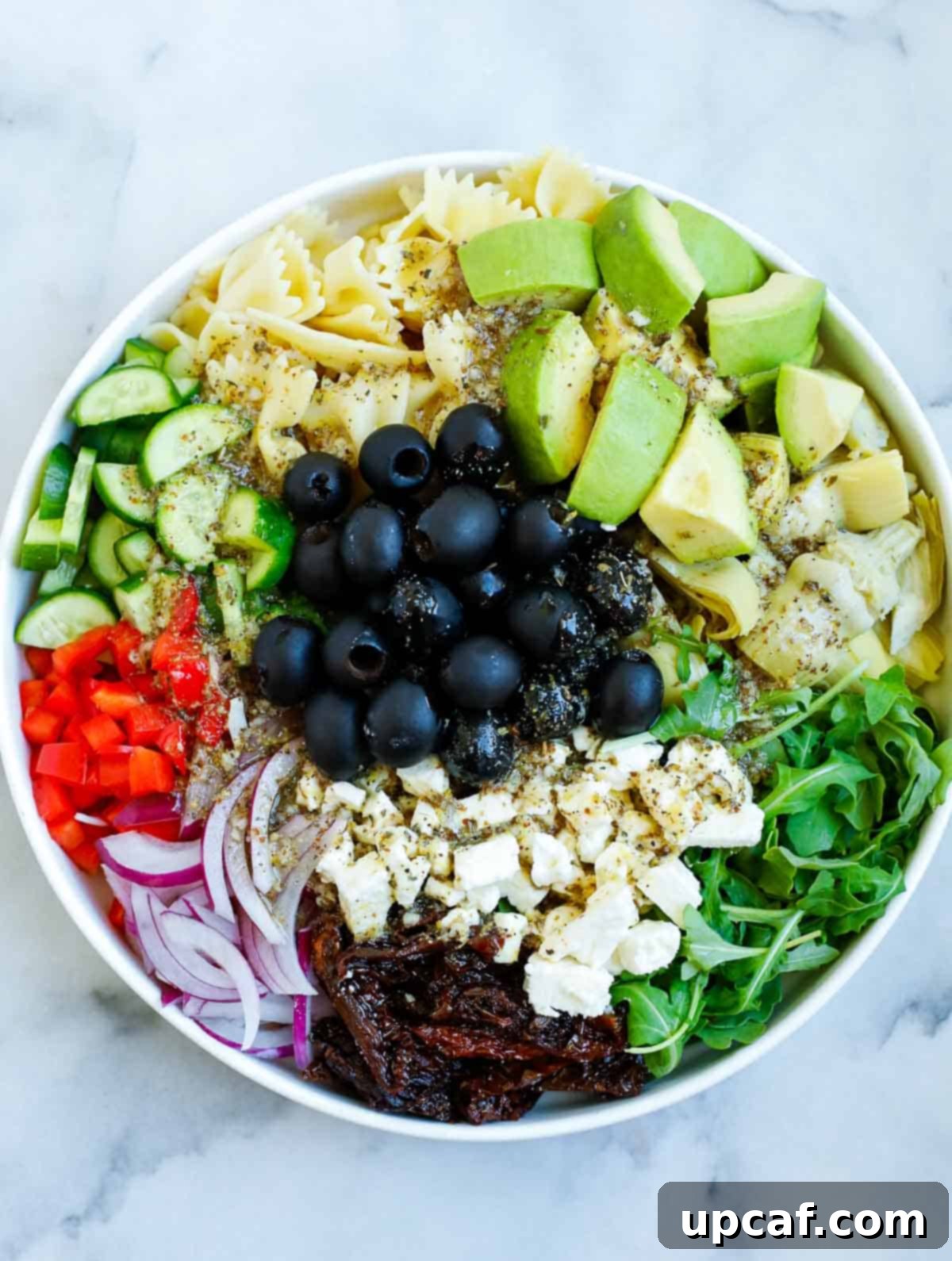 Zesty lemon herb dressing being poured over a bowl of fresh Mediterranean pasta salad ingredients.