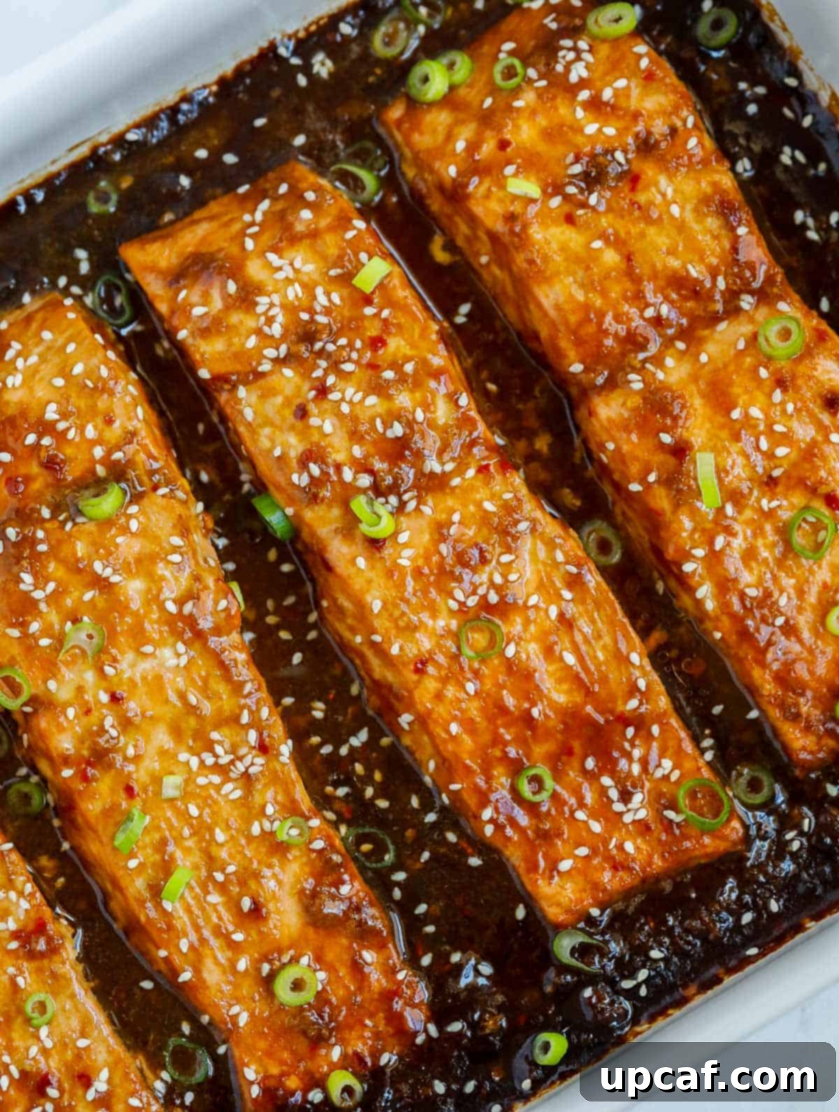 Sweet & Sticky Teriyaki Salmon 2 Baked teriyaki salmon glistening in a baking dish, garnished with green onions and sesame seeds.