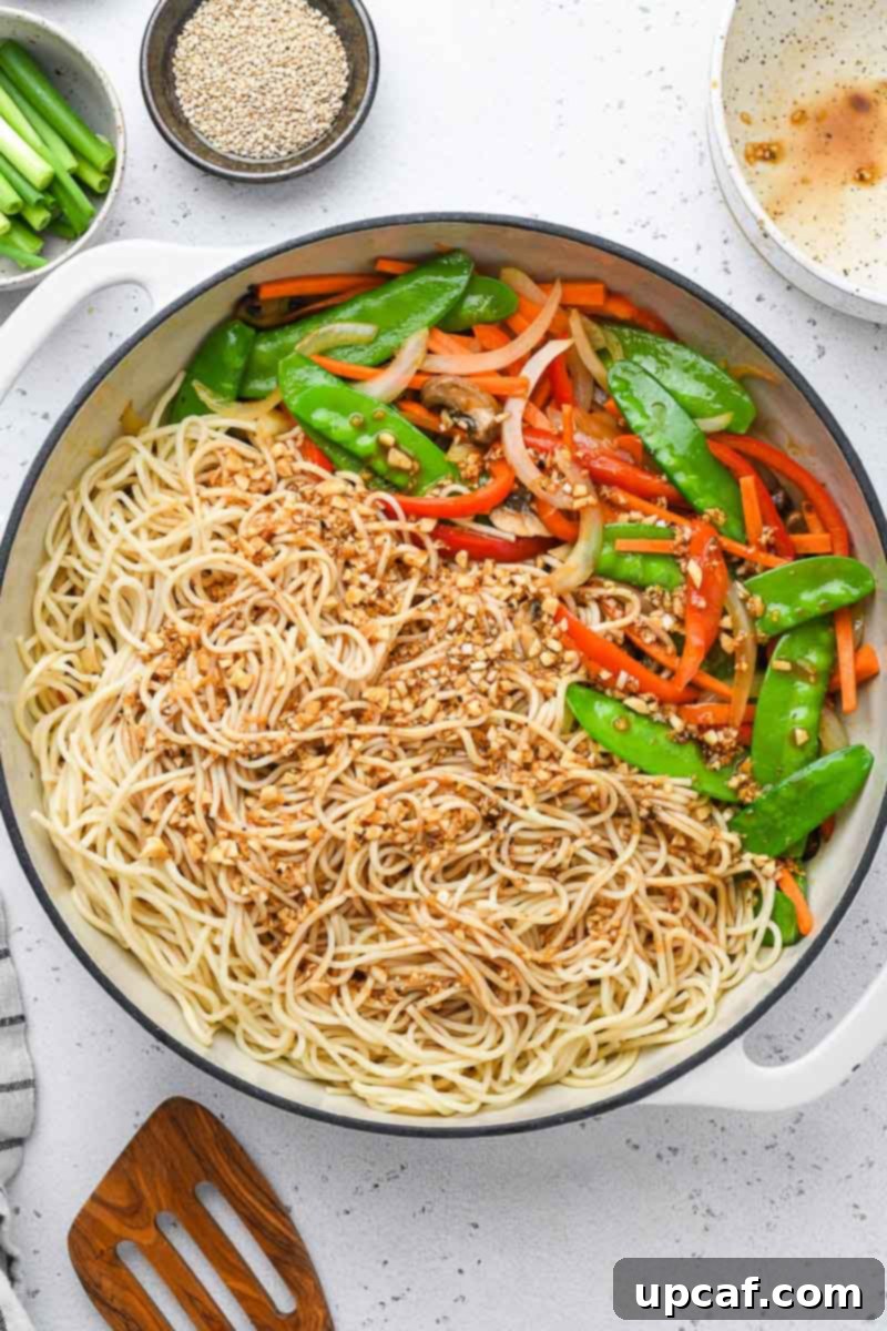 The savory lo mein sauce being poured over stir-fried noodles and vegetables in a wok.