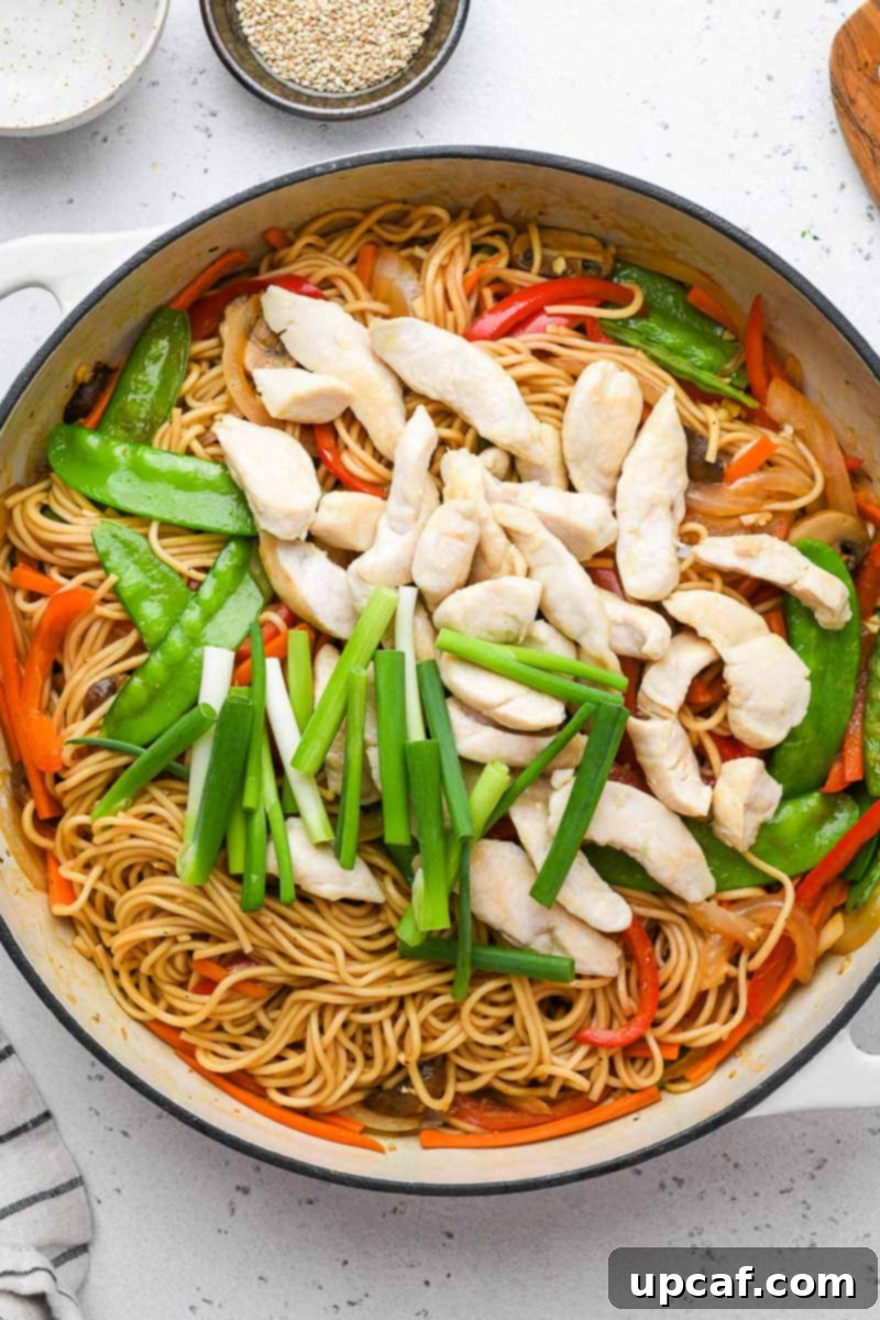 Cooked chicken and vegetables mixed with lo mein noodles in a large skillet.