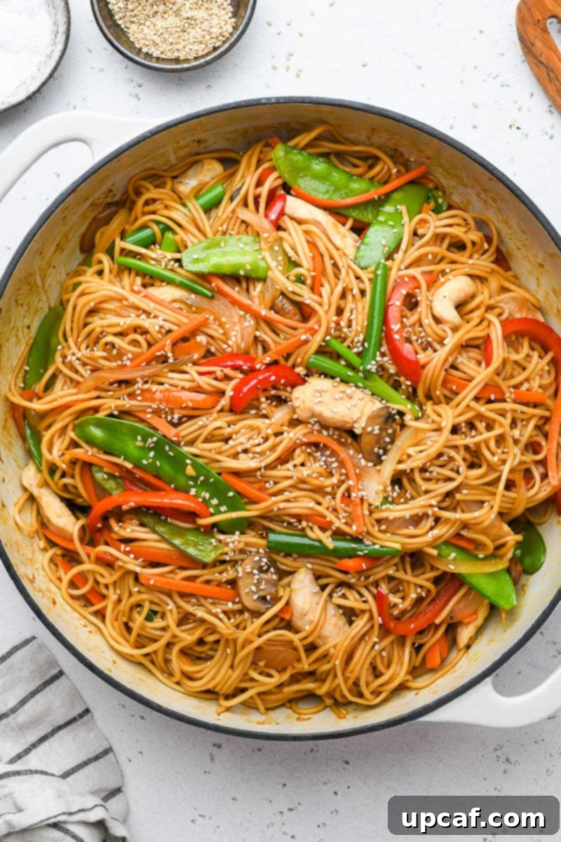 A large skillet filled with freshly made chicken lo mein, garnished with sesame seeds.