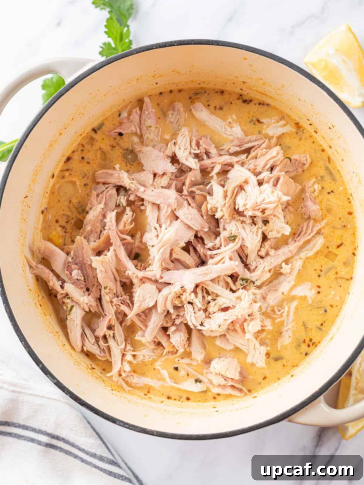 Close-up of the easy white chicken chili simmering in a pot after the shredded chicken has been added, creating a rich, creamy texture.