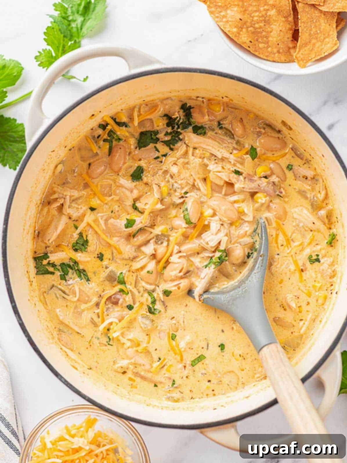 A large pot filled with cooked creamy white chicken chili, with a spoon resting in the rich, inviting soup.