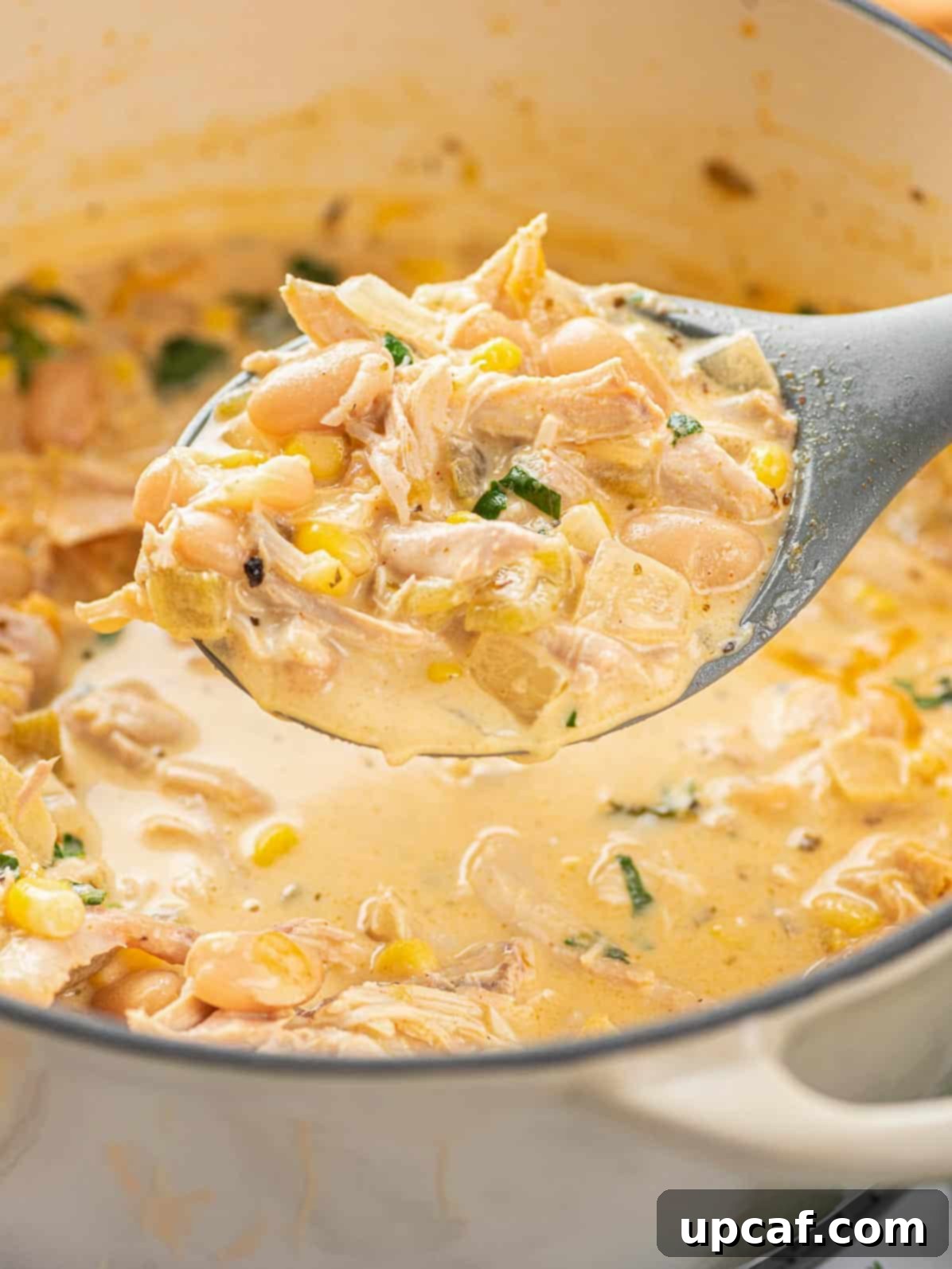 A serving spoon lifting a spoonful of rich, creamy white chicken chili from a pot, showcasing its hearty ingredients.