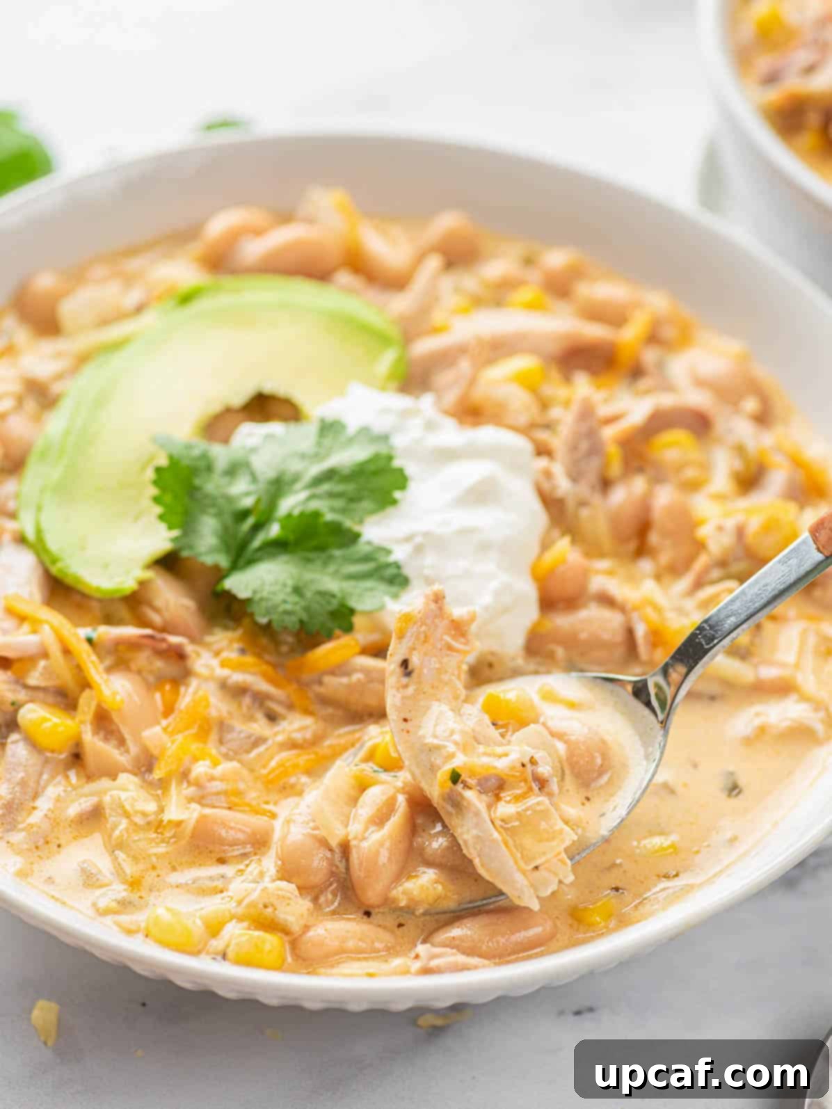 A close-up shot of a spoon scooping creamy white chicken chili from a white plate, highlighting the rich texture and ingredients.