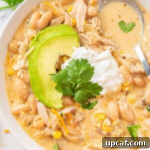 A bowl of creamy white chicken chili, garnished with sour cream and avocado.