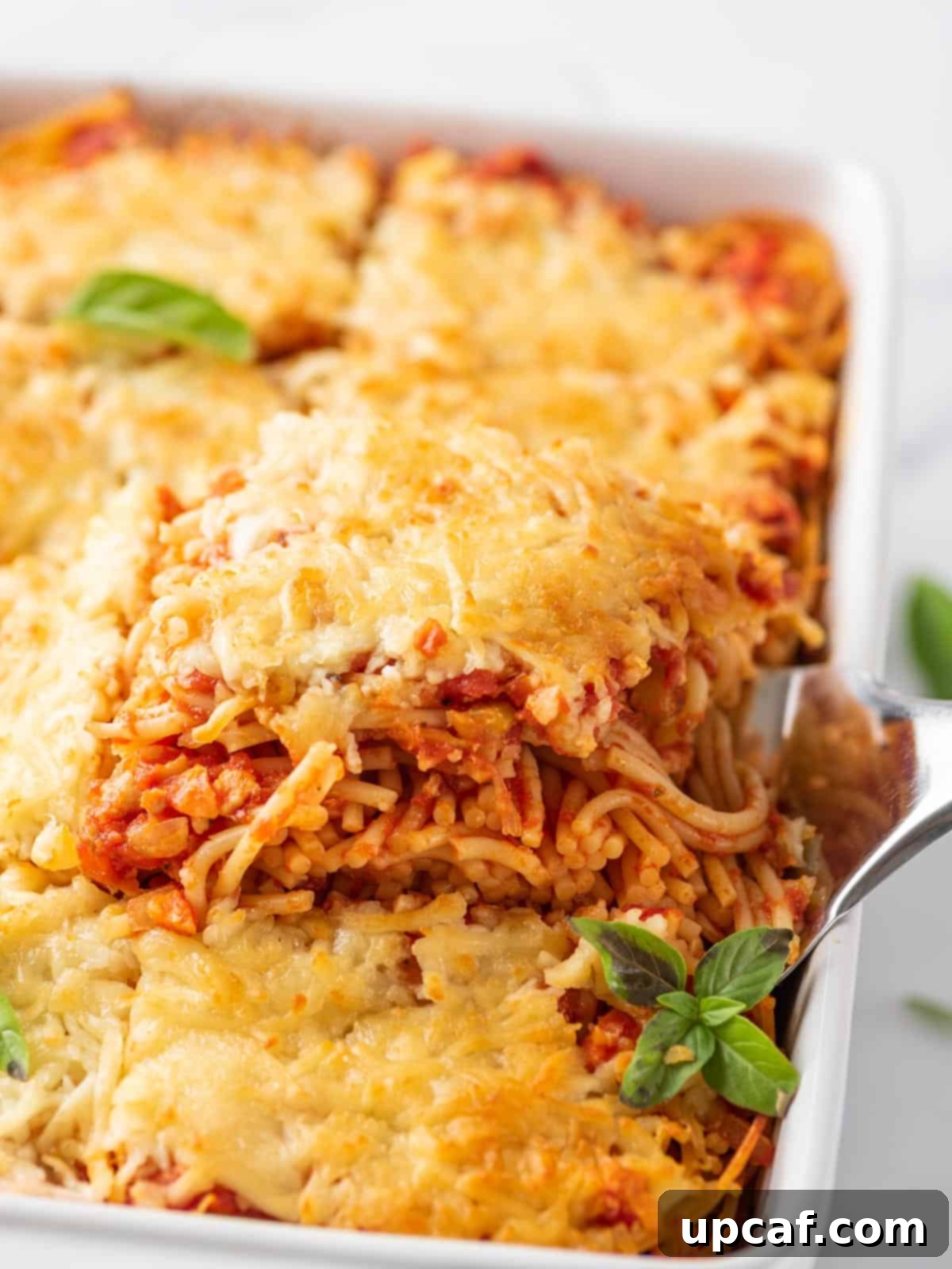 Spatula lifting out a portion of the baked spaghetti, showcasing the layers of pasta, sauce, and melted cheese.