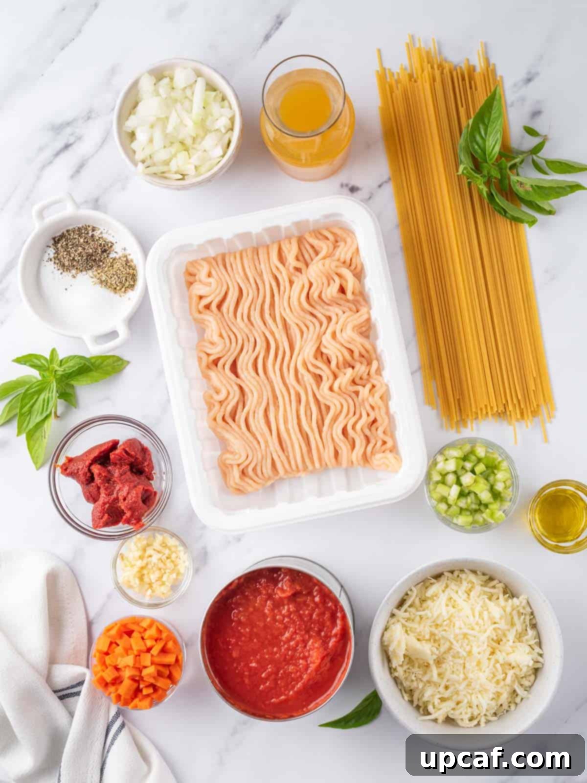 A vibrant display of fresh ingredients for baked spaghetti, including vegetables, ground chicken, canned tomatoes, and spices.