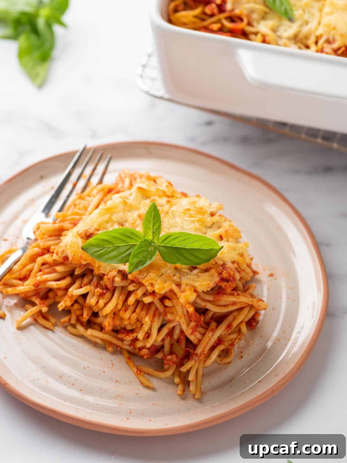 A delicious portion of baked spaghetti pasta served on a white plate, adorned with fresh basil leaves for a final touch.
