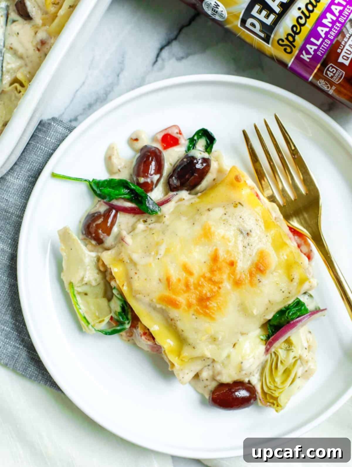 Piece of Greek White Alfredo Lasagna Roll on a plate with a gold fork