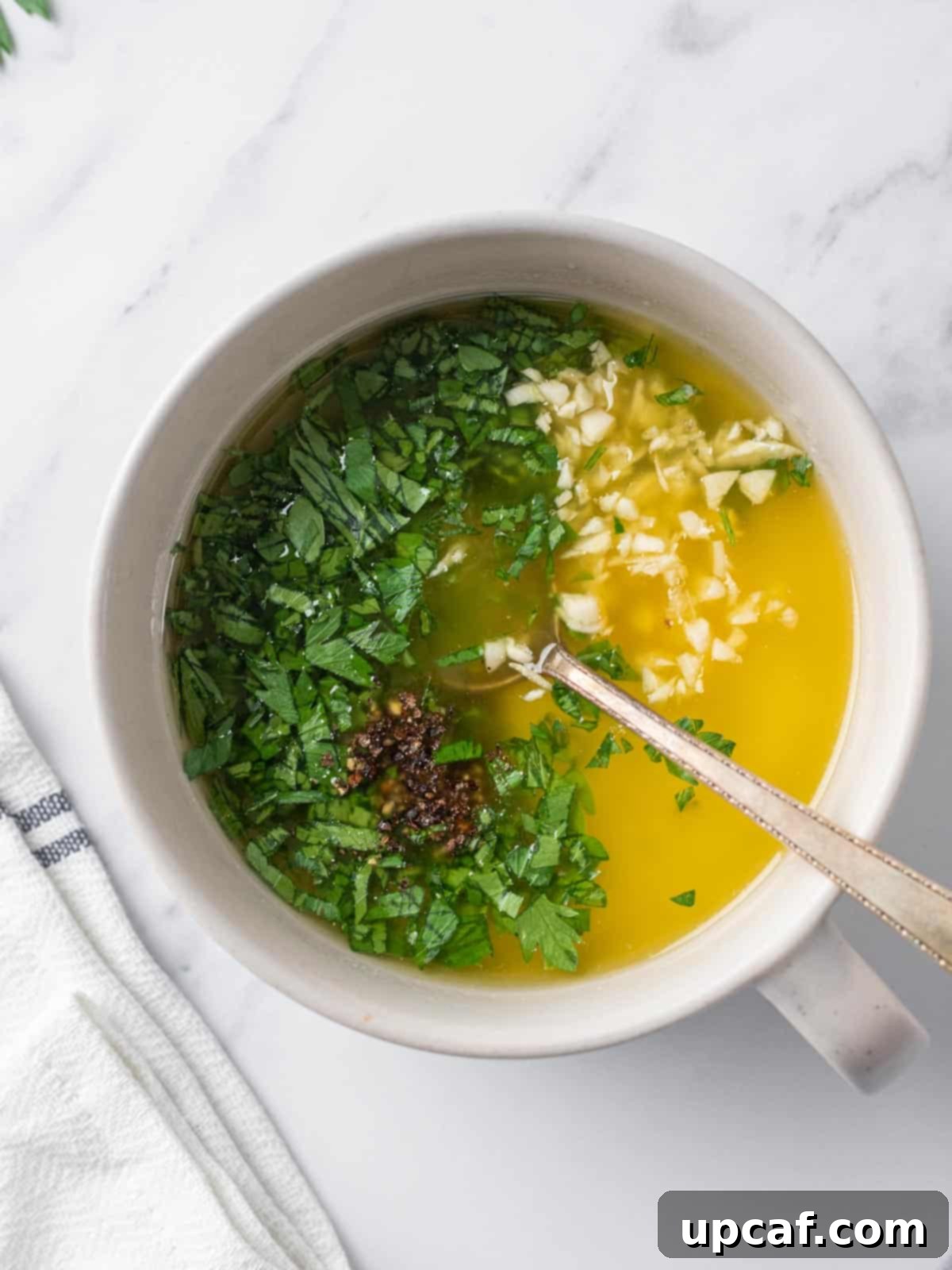 A small bowl of garlic butter sauce with fresh parsley being stirred.