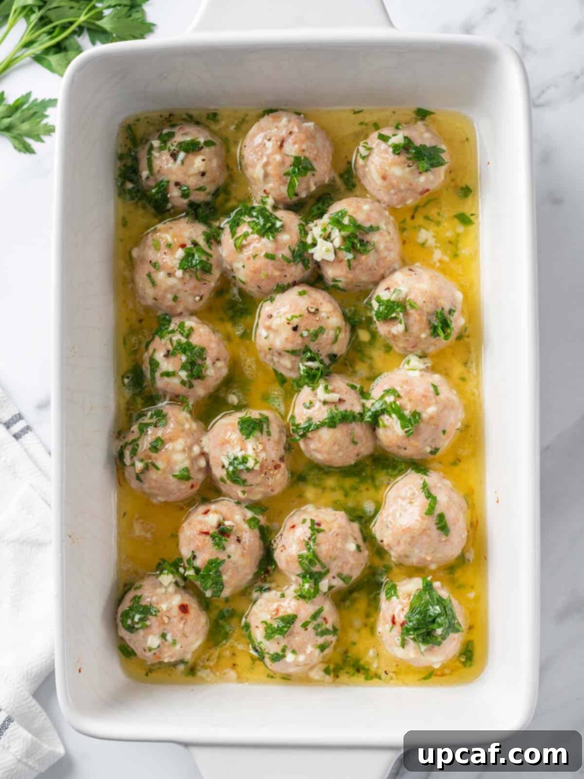 Garlic butter sauce being poured generously over semi-baked turkey meatballs in a baking dish.