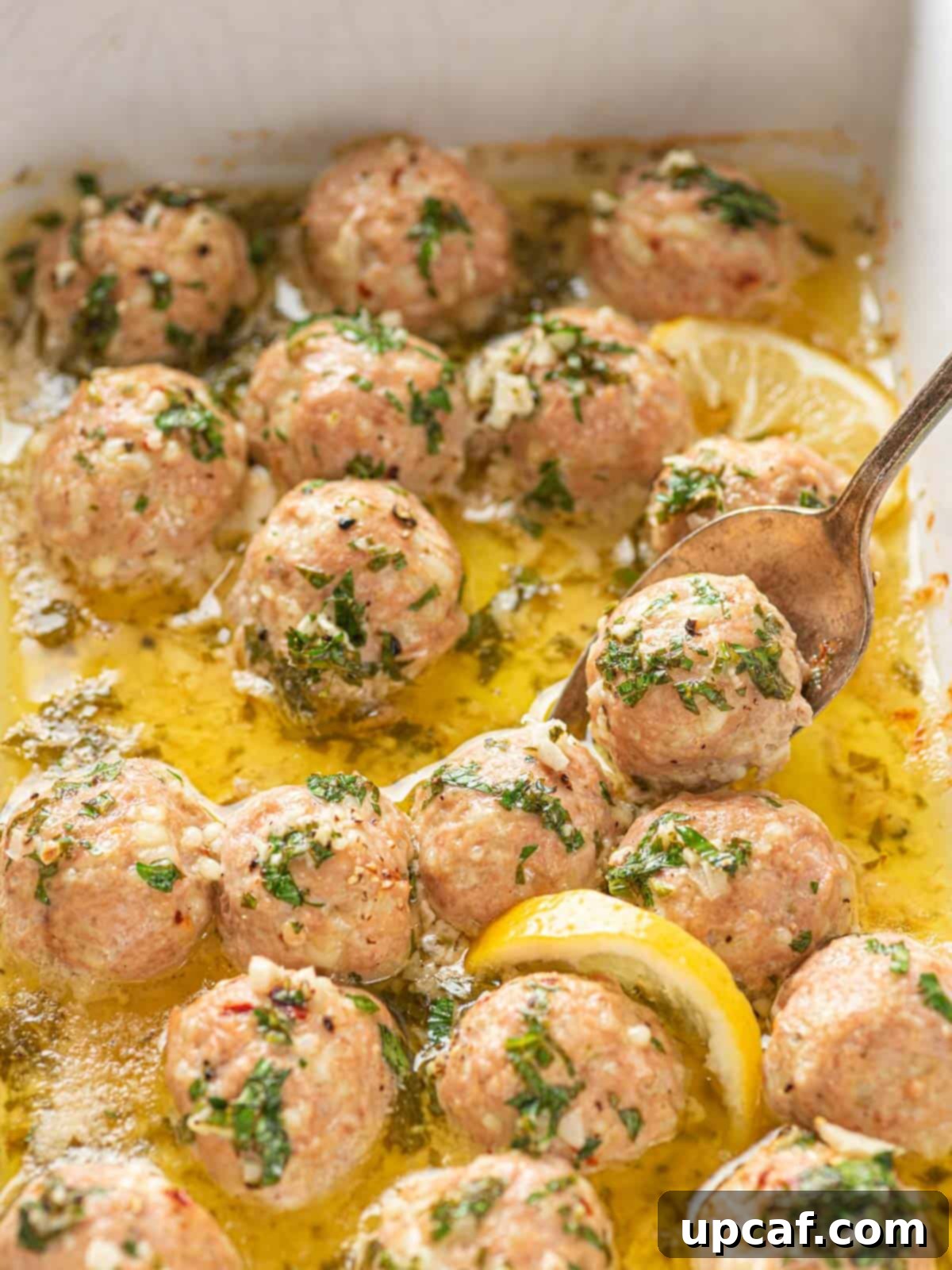 Finished Garlic Butter Turkey Meatballs in a baking dish, with one being scooped out onto a serving plate.