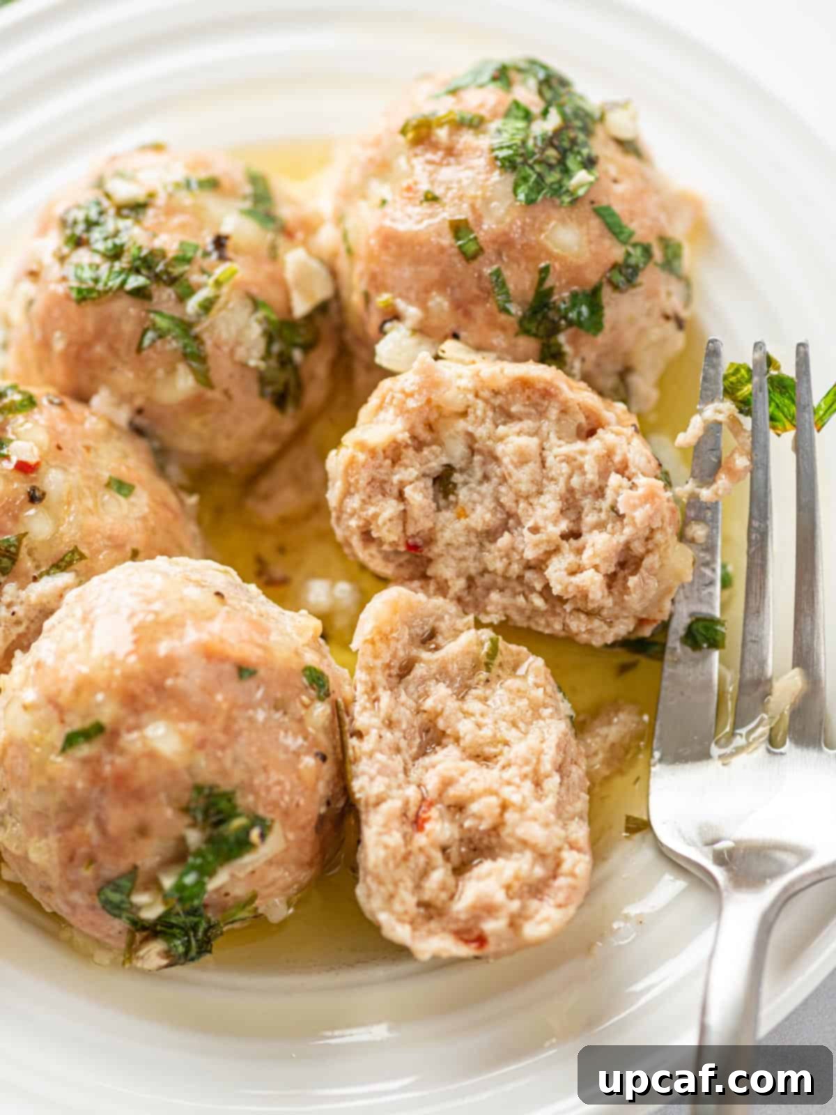 Perfectly cooked turkey meatballs on a plate, with one cut in half to show its juicy interior.