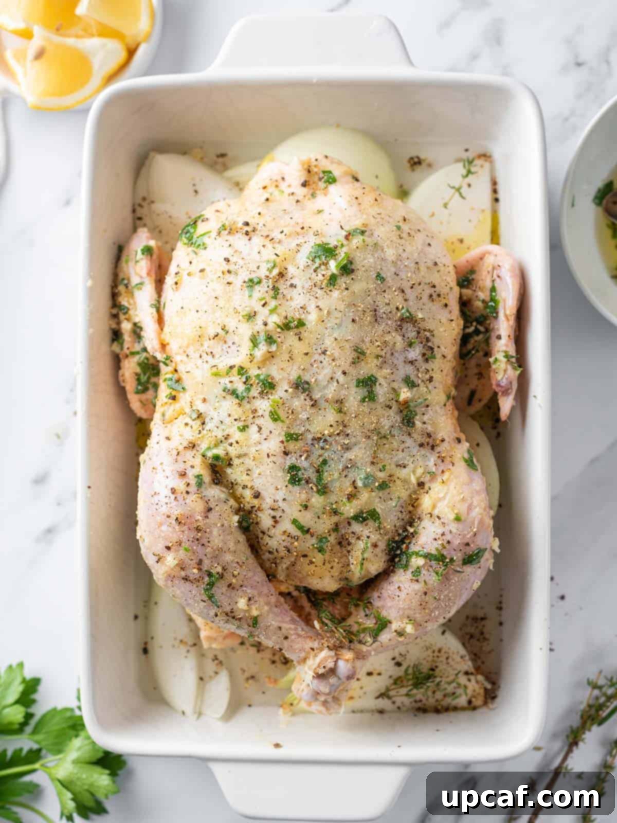 A whole chicken expertly rubbed with a fragrant herb and butter mixture, placed in a roasting pan with onion wedges.