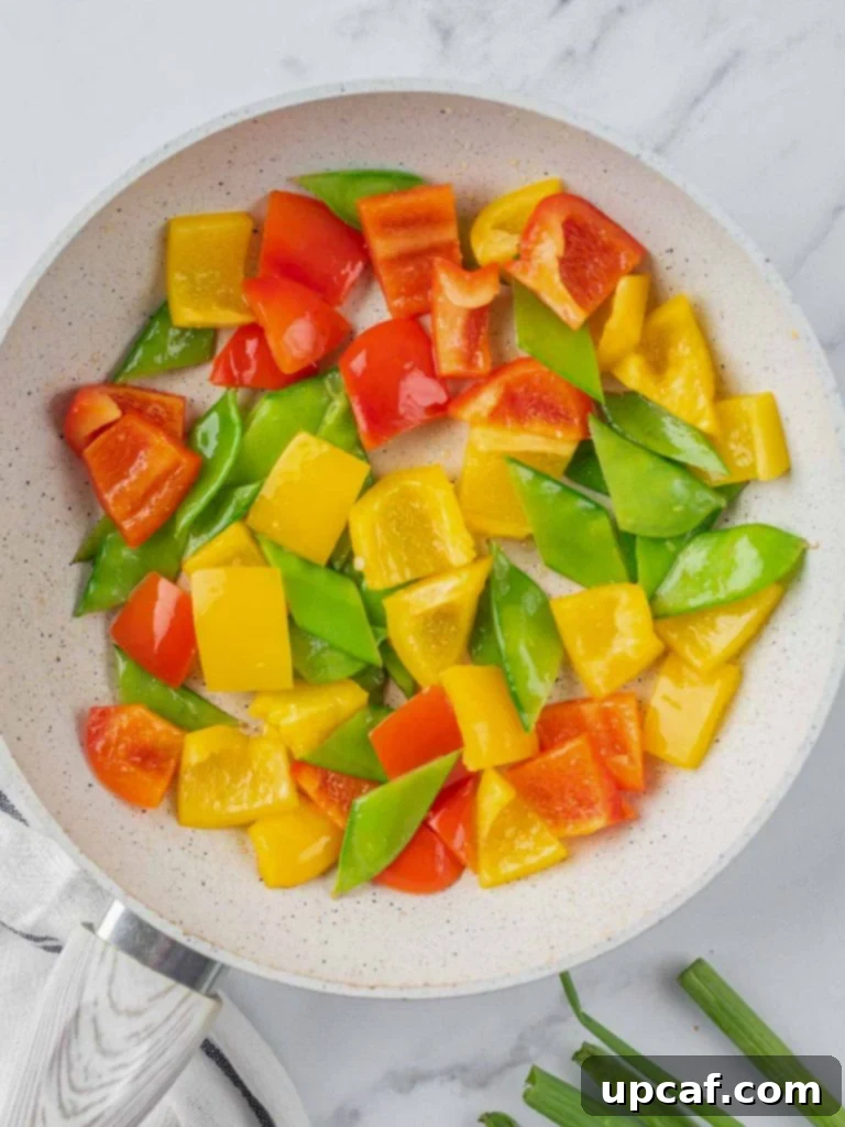 Vibrant bell peppers and crisp snow peas stir-frying in a hot pan.