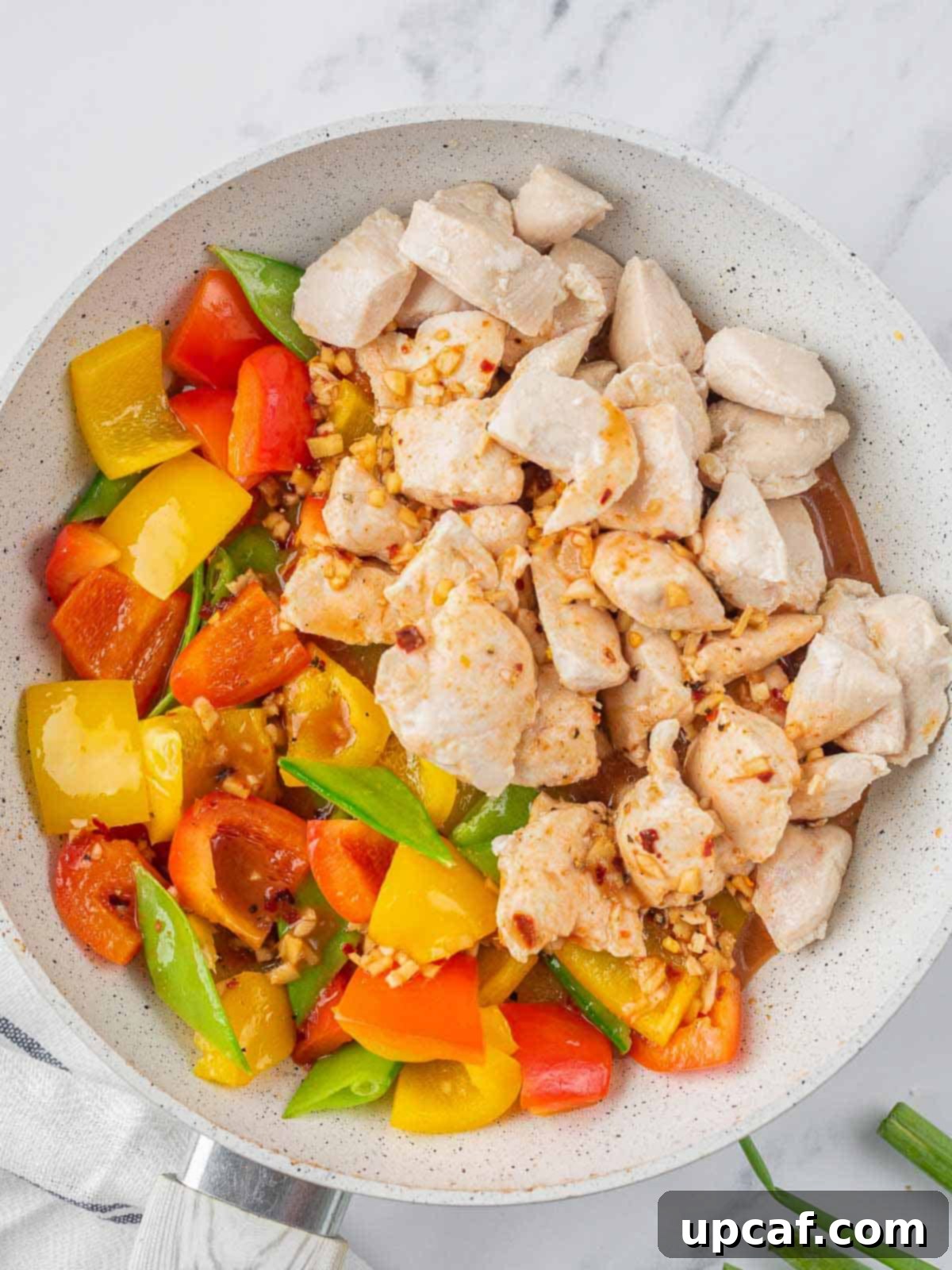 Partially cooked chicken being added back to a pan of colorful stir-fried vegetables.