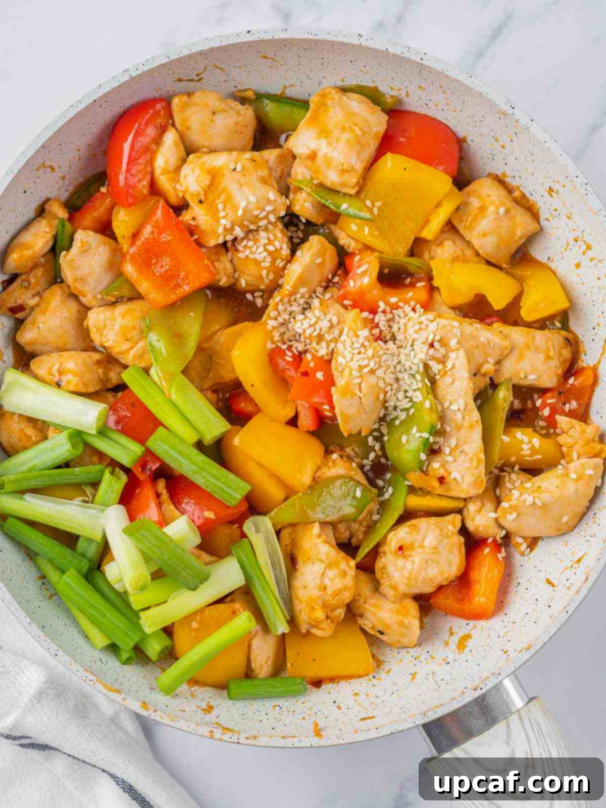 Fresh green onions and sesame seeds being added to the finished Szechuan chicken stir-fry.