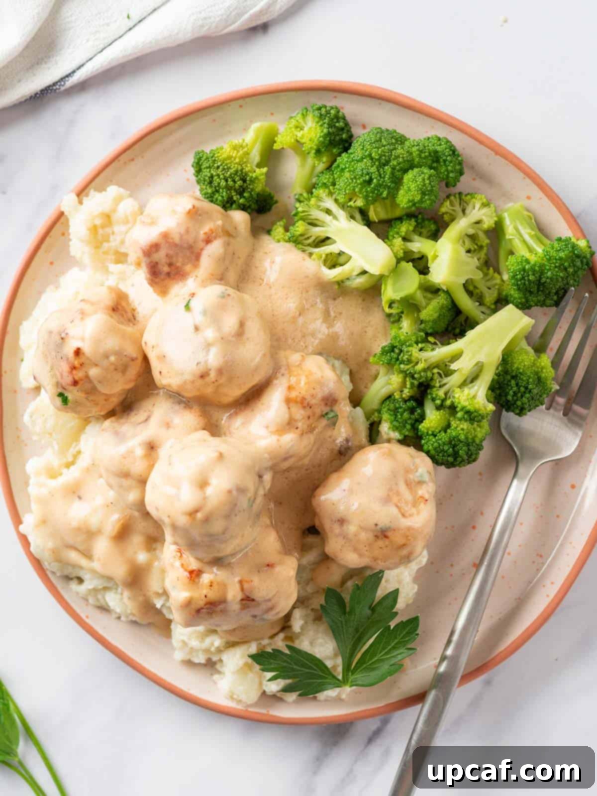 A plate of Swedish chicken meatballs with creamy mashed potatoes and vibrant green broccoli florets.