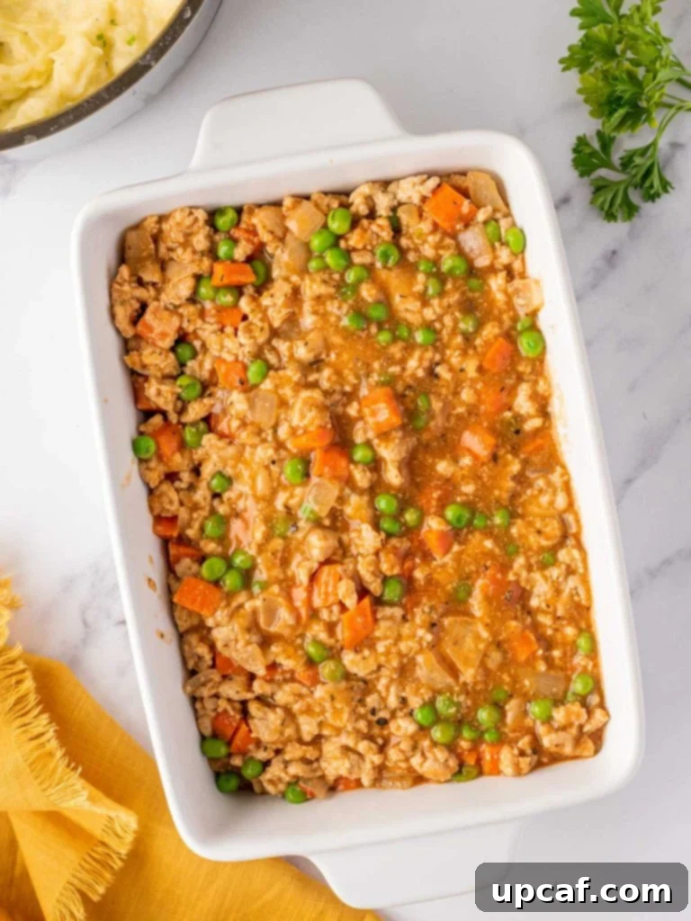 The chicken and vegetable filling spread evenly in a rectangular baking dish, awaiting the mashed potato topping.