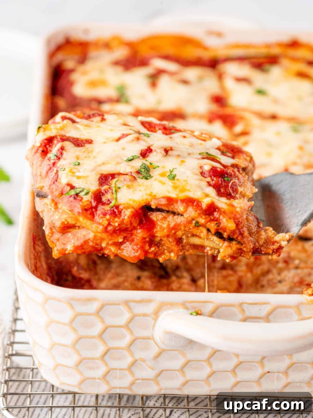 A generous piece of golden-brown Eggplant Parmesan Lasagna being scooped up with a spatula from a baking dish, revealing its creamy layers.