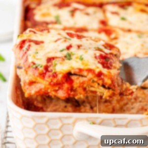 A generous piece of golden-brown Eggplant Parmesan Lasagna being scooped up with a spatula from a baking dish, revealing its creamy layers.