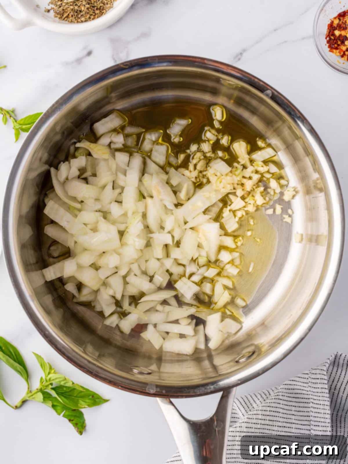 Chopped yellow onions and minced garlic gently sautéing in olive oil within a saucepan, forming the aromatic base for the marinara sauce.