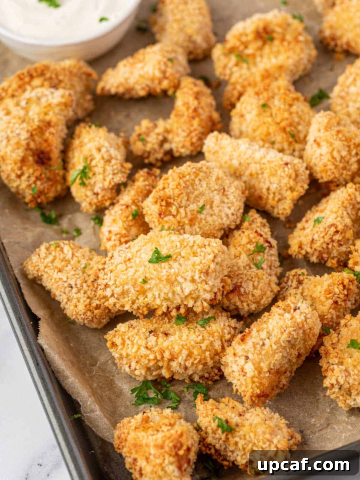 A large pile of crispy, golden-brown popcorn chicken pieces arranged on a baking sheet, ready to serve.