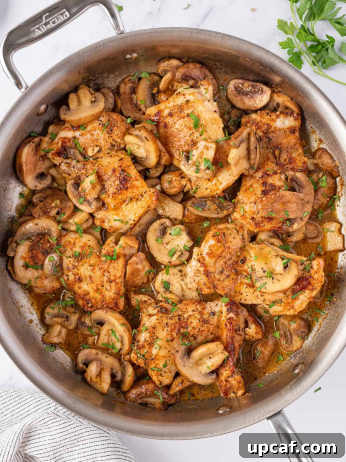 Flavorful Garlic Mushroom Chicken Thighs 7 Cooked chicken thighs resting among sautéed garlic butter mushrooms in a skillet, ready to be garnished.