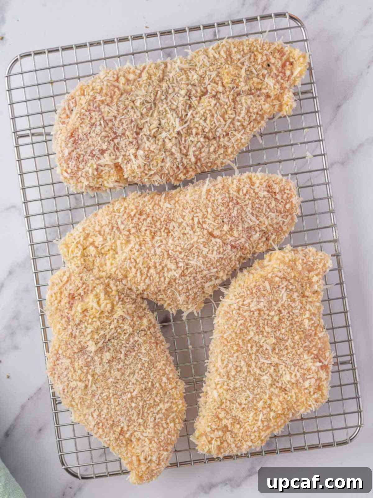 Coated chicken breasts resting on a wire rack.
