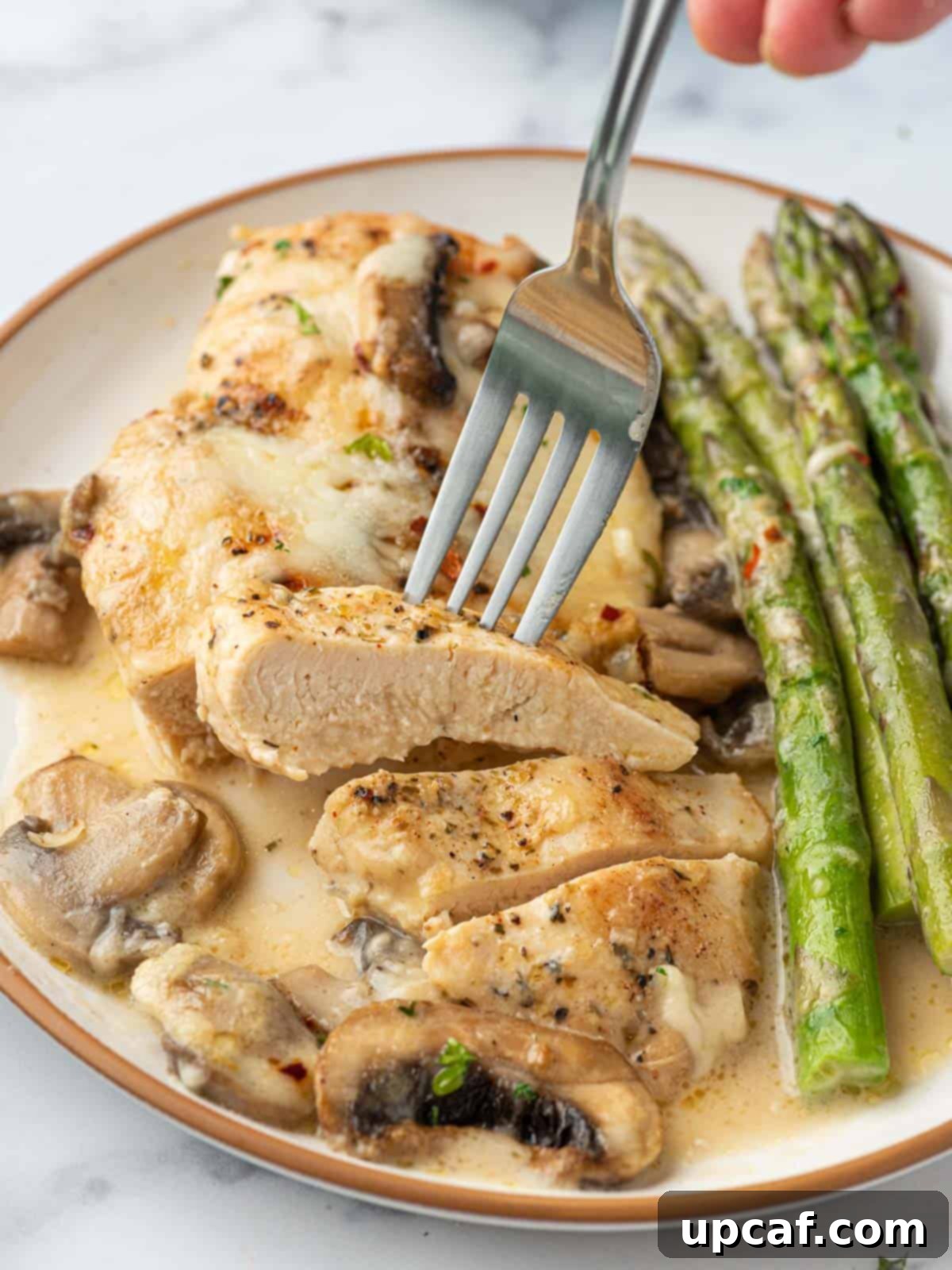 A stunning close-up of a plate of homemade Chicken Madeira, featuring perfectly cooked chicken, a generous portion of mushrooms and asparagus, all covered in the irresistible creamy, cheesy sauce.