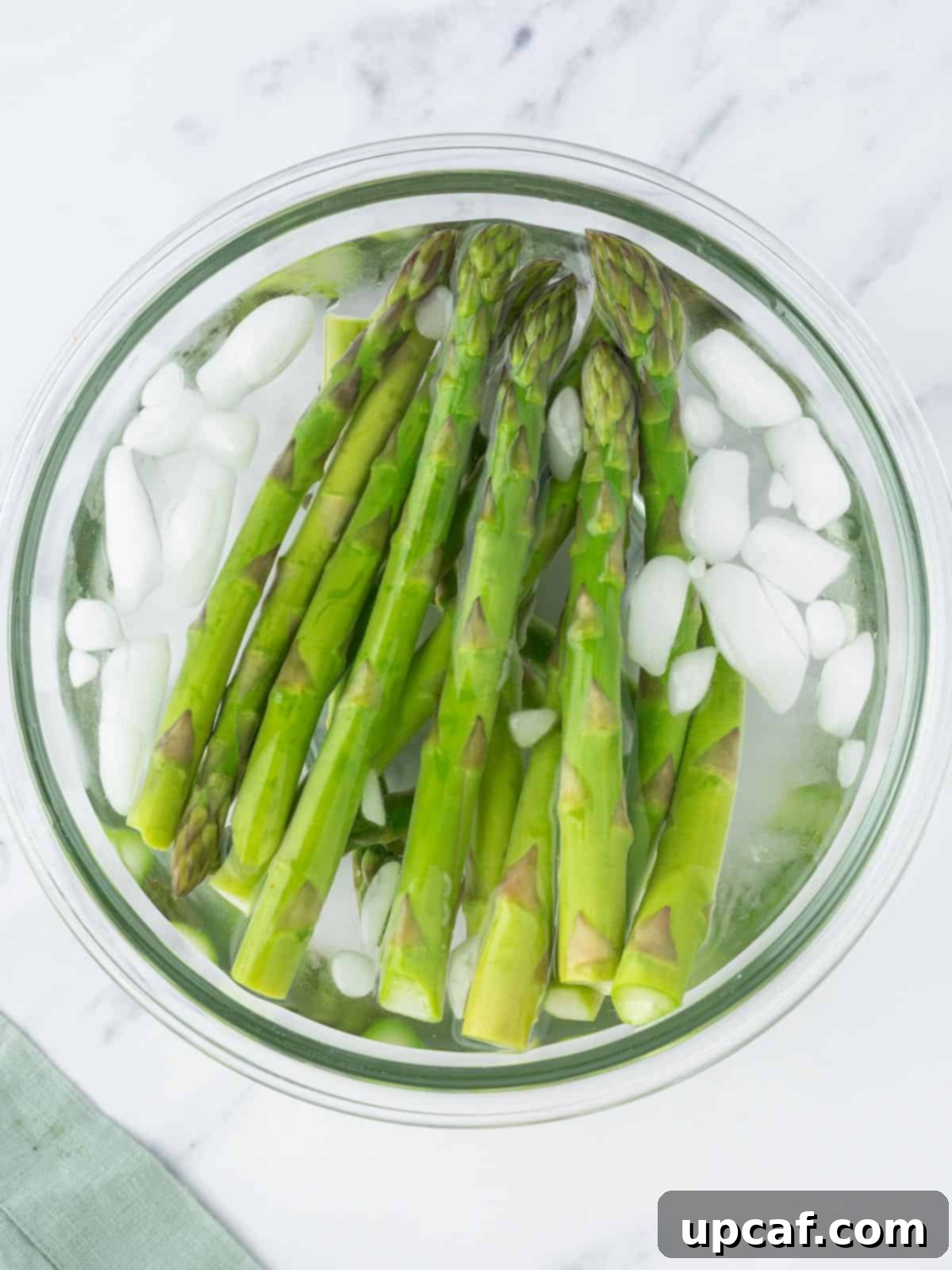 Blanched asparagus spears being transferred into an ice bath to preserve their color and crispness.