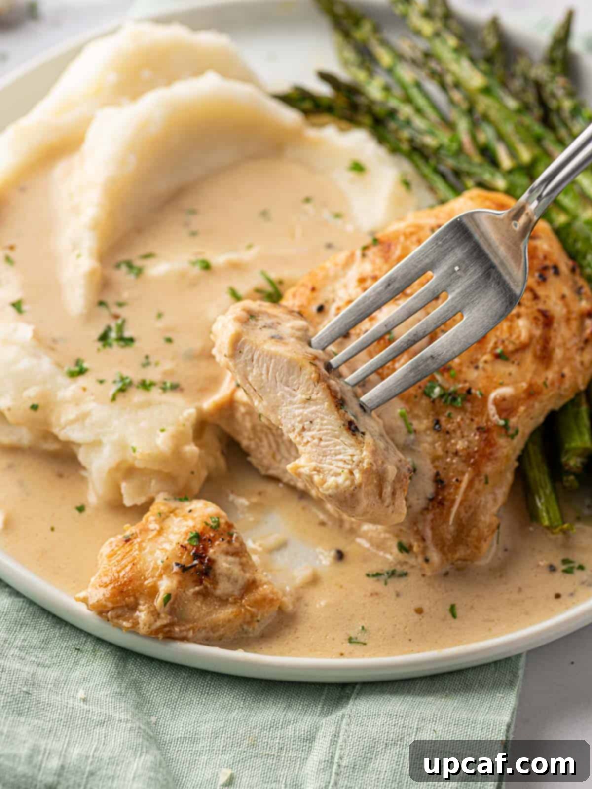 A tantalizing close-up shot of a tender piece of creamy parmesan chicken being lifted from a serving dish, showcasing the rich sauce and a sprinkle of fresh herbs.