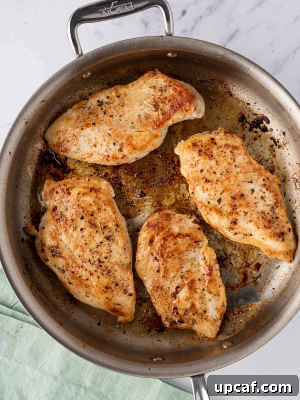 A large skillet containing four perfectly cooked, golden-brown chicken breasts, still glistening from the pan, ready to be removed.