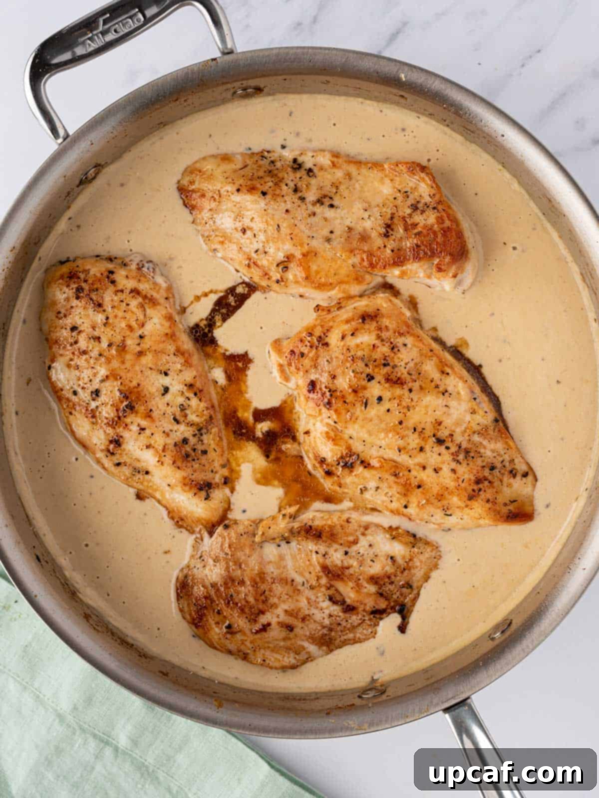 Golden-brown chicken breasts nestled invitingly in a rich, creamy garlic parmesan sauce within a skillet, ready to finish cooking.