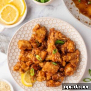 A white plate with Asian Lemon Chicken and a fresh lemon wedge. A bowl of fresh lemons is off to the side.