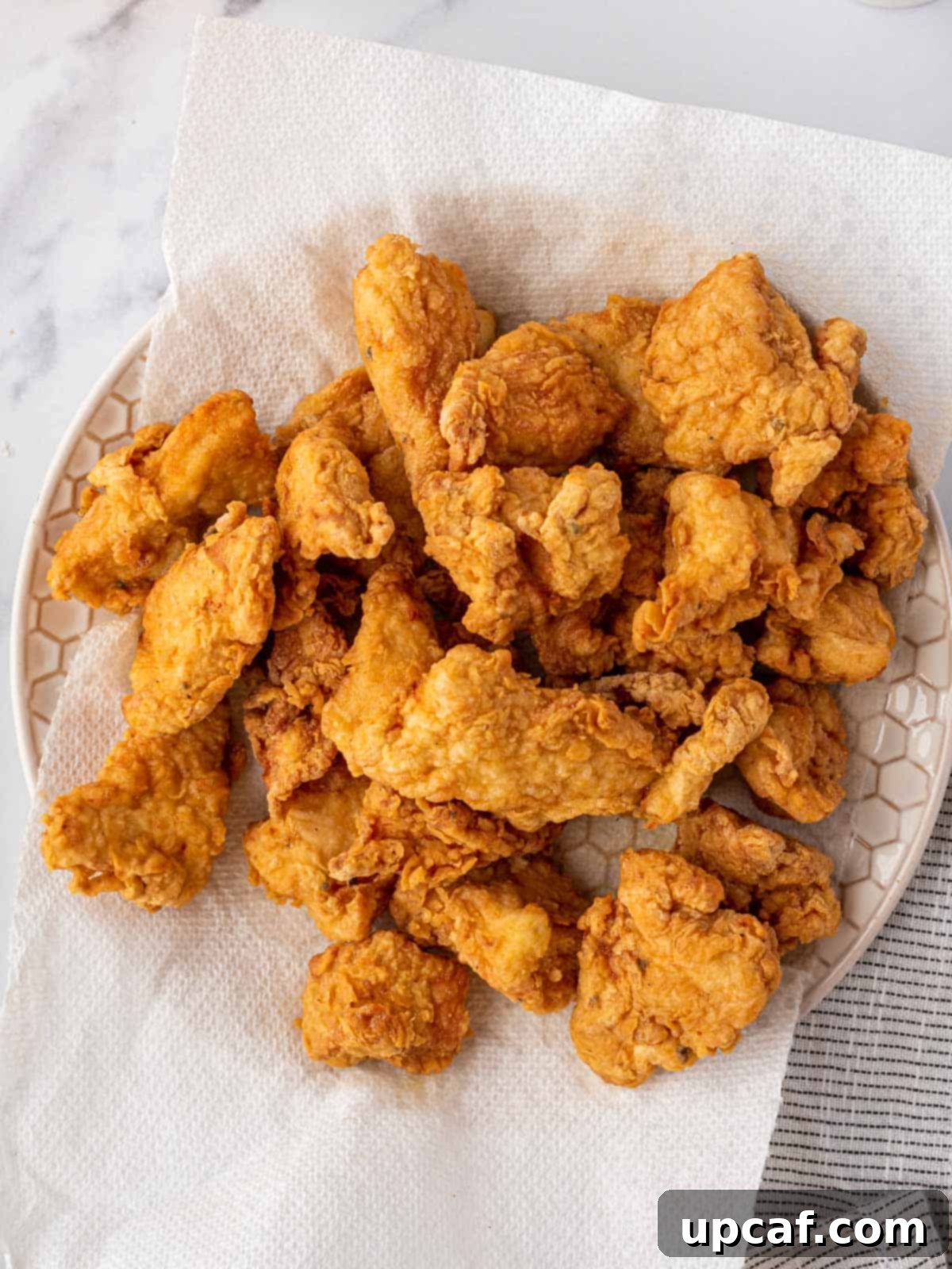 Crispy deep-fried chicken pieces draining on a paper towel-lined wire rack.