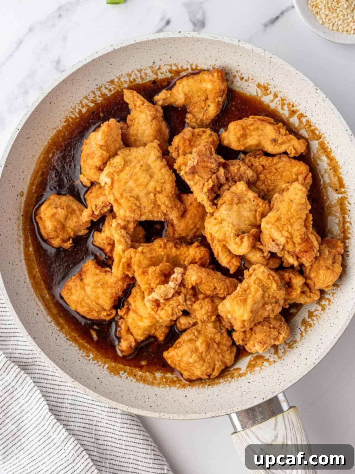 Crispy fried chicken pieces submerged in a glistening Chinese lemon sauce in a large skillet.
