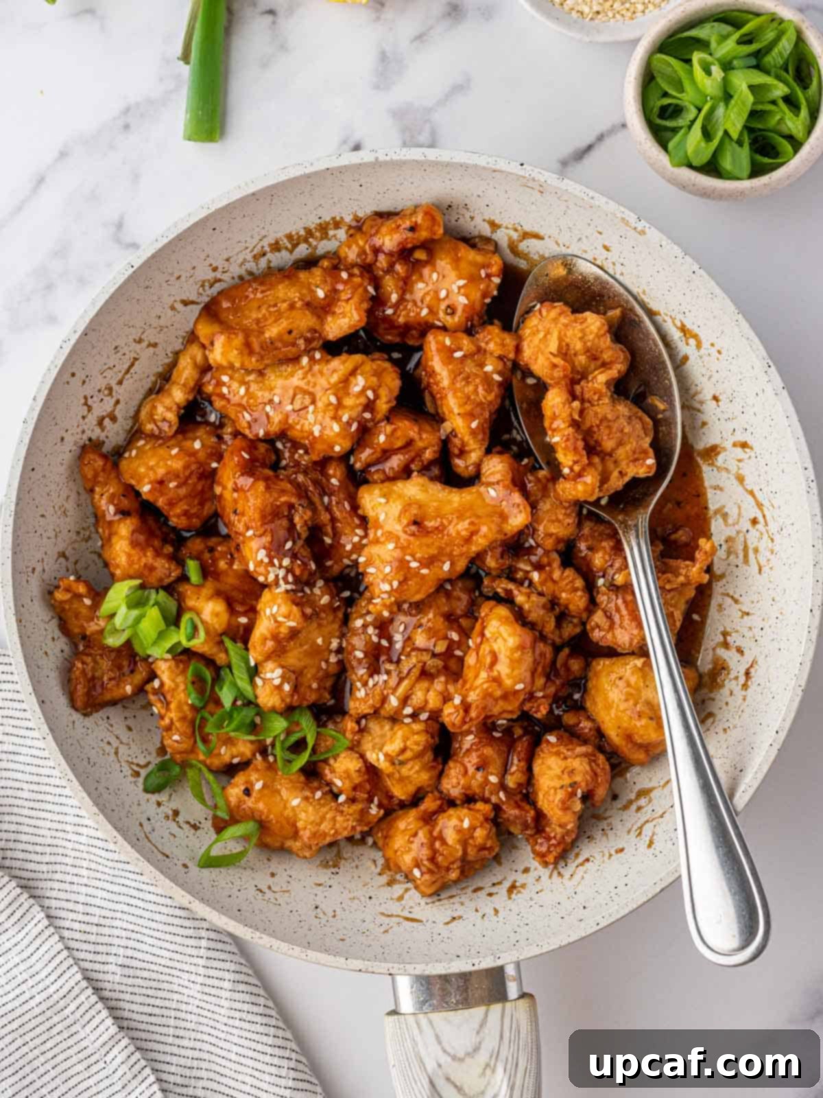 A large serving bowl filled with a generous portion of Asian lemon chicken, accompanied by a serving spoon.