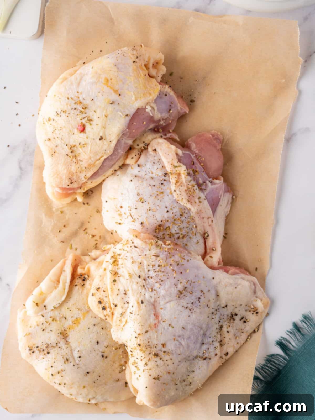 Bone in skin on chicken thighs with seasoning on parchment paper, ready for searing.
