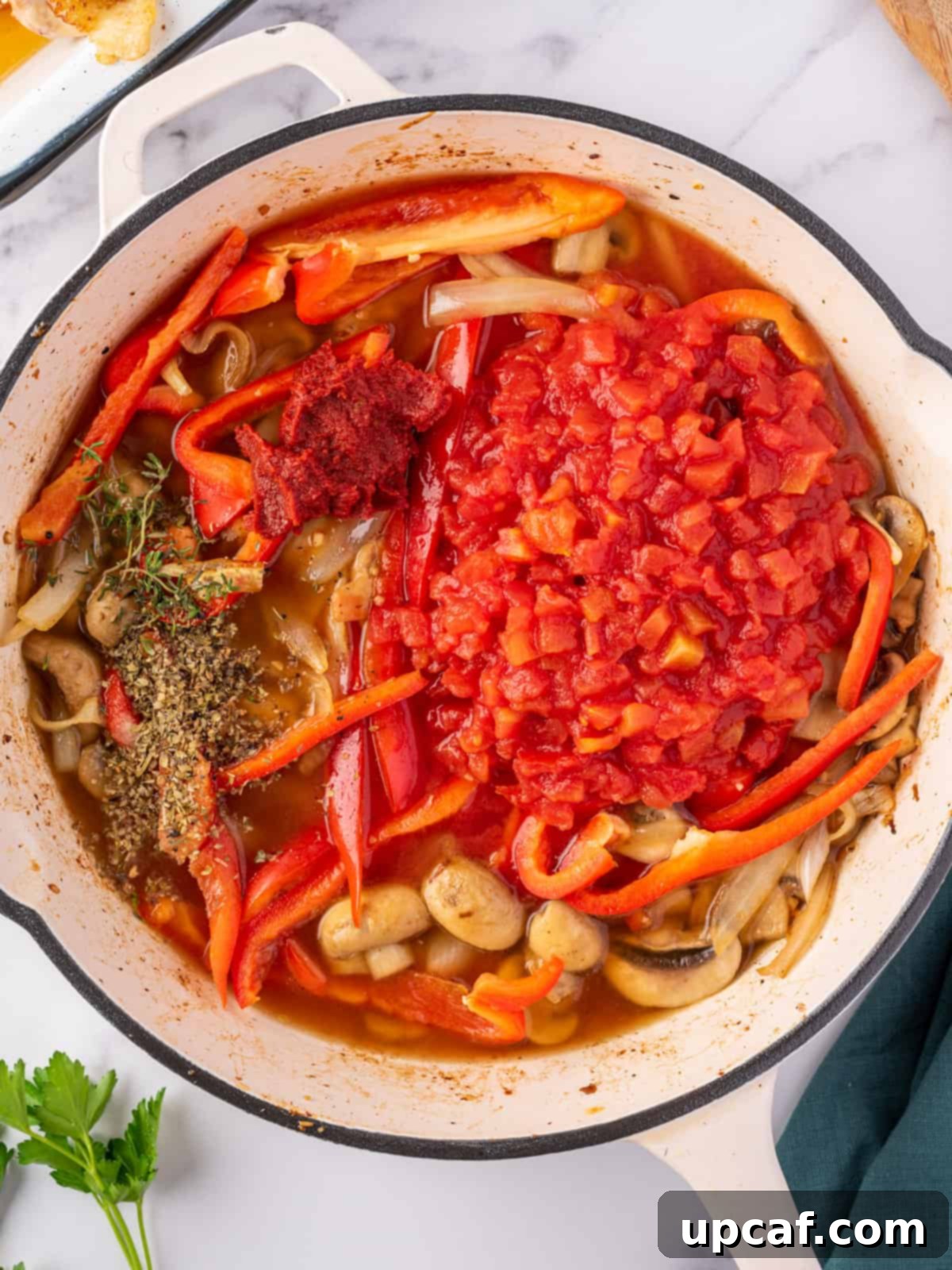 Process of making the sauce for the best chicken cacciatore, with tomatoes, herbs, and stock simmering.