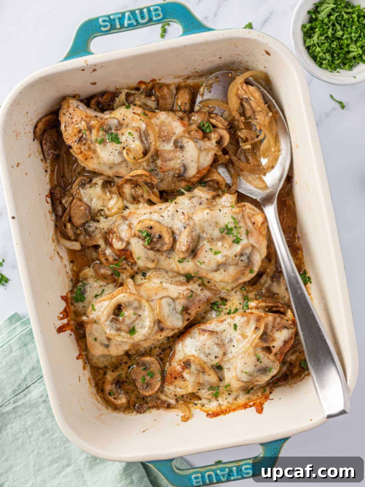 Close-up of baked mushroom chicken in a baking dish with a serving spoon, showcasing the melted cheese and juicy chicken.