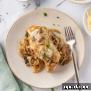 Overhead view of a plate of cheesy baked chicken breasts with mushrooms with a fork on the plate.