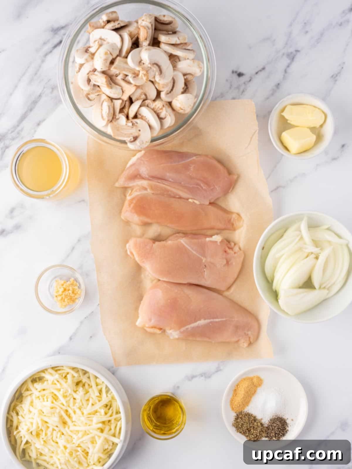 A selection of fresh ingredients laid out, including chicken breasts, mushrooms, onion, garlic, olive oil, butter, and seasonings.